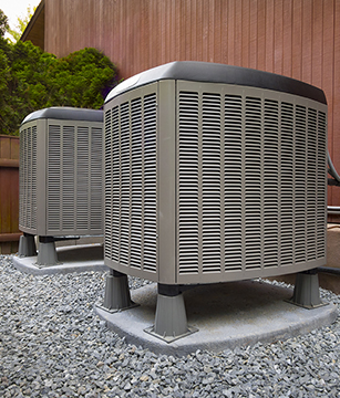 Photo of two heat pump units surrounded by gravel outside of a home