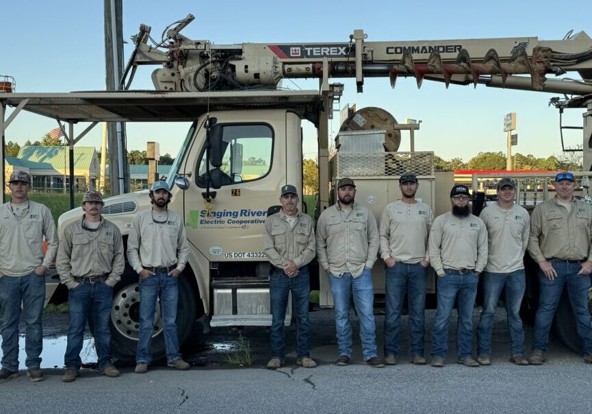 Linemen stand in front of a company truck