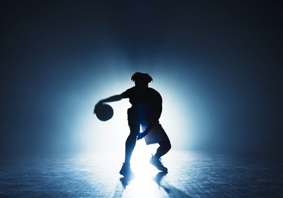 Silhouette of male basketball player dribbling basketball while playing on sports court during practice.