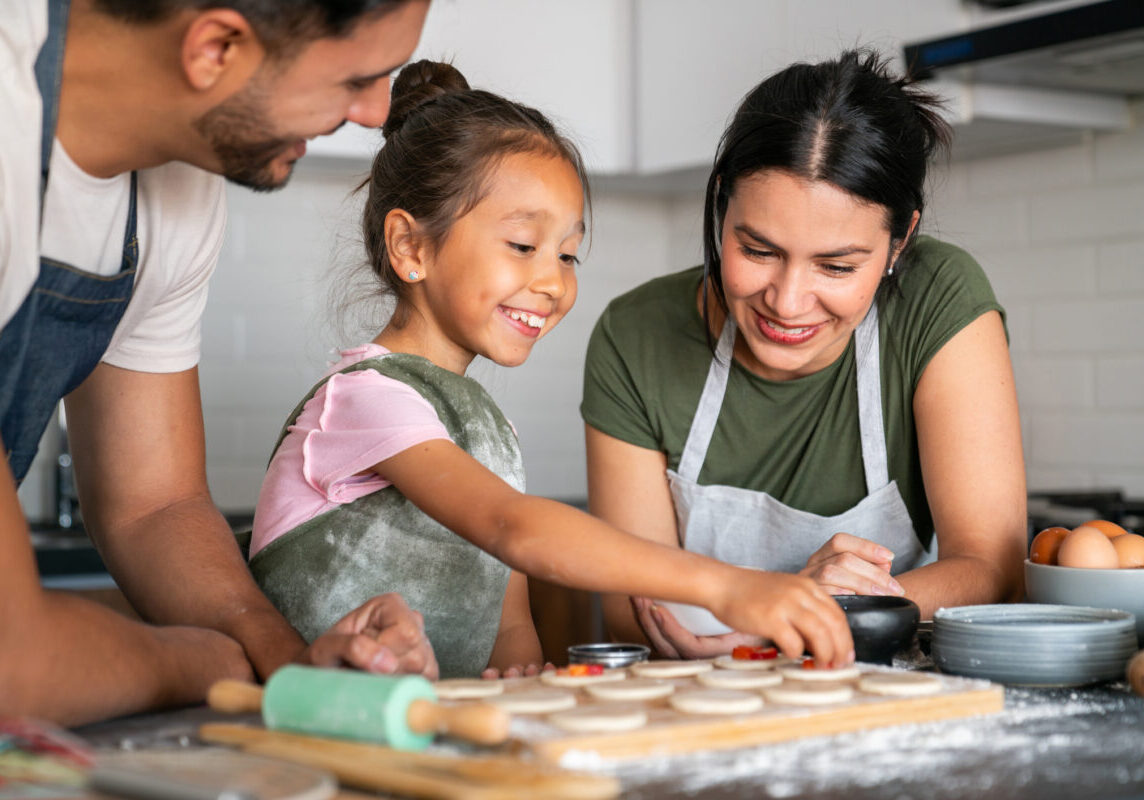 Happy Latin American girl baking at home with her loving parents - family lifestyle concepts