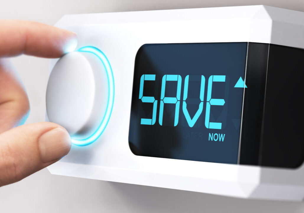 Hand turning a thermostat knob to increase savings by decreasing energy consumption. Composite image between a hand photography and a 3D background.